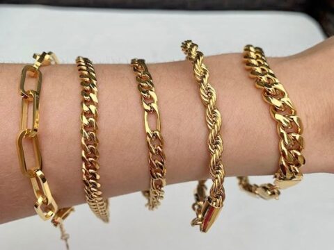 Fem olika guldfärgade kedjearmband på en arm.