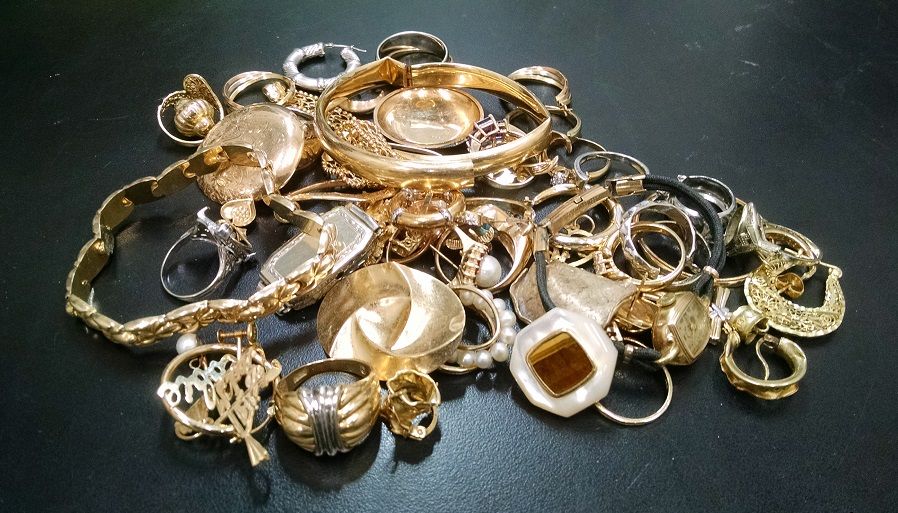 En hög med vintage guldsmycken och armband på en mörk yta.